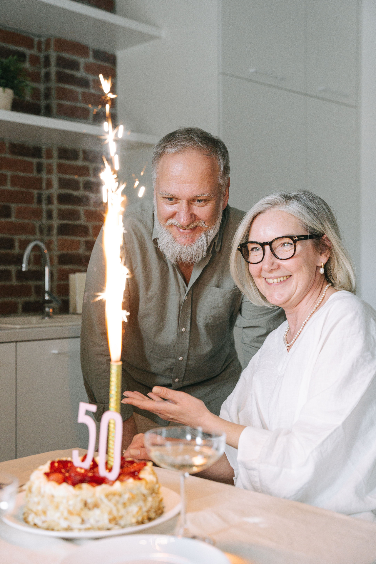 Smiling older couple celebrating with a strawberry cake and a sparkler candle marked 50