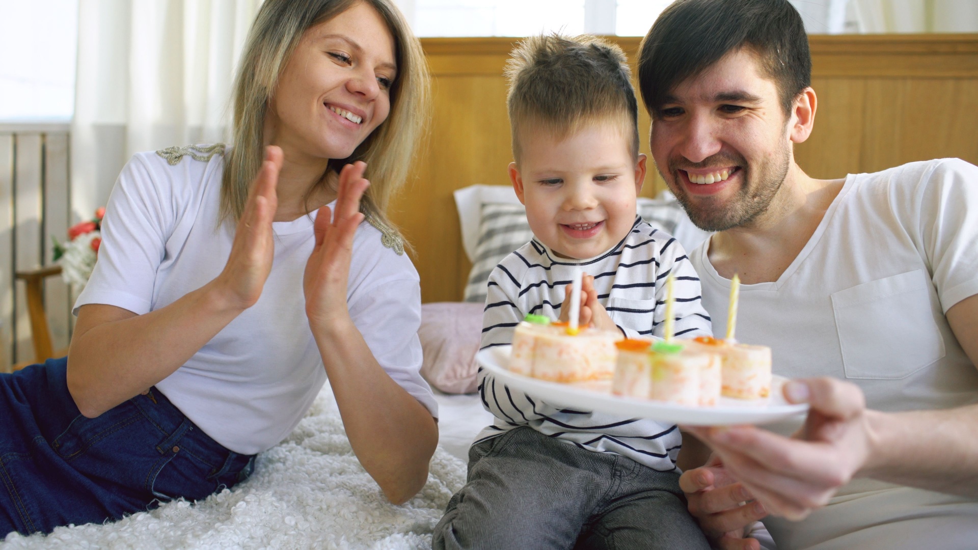 Mum, dad and toddler son laughing together over a plate of small celebration cakes
